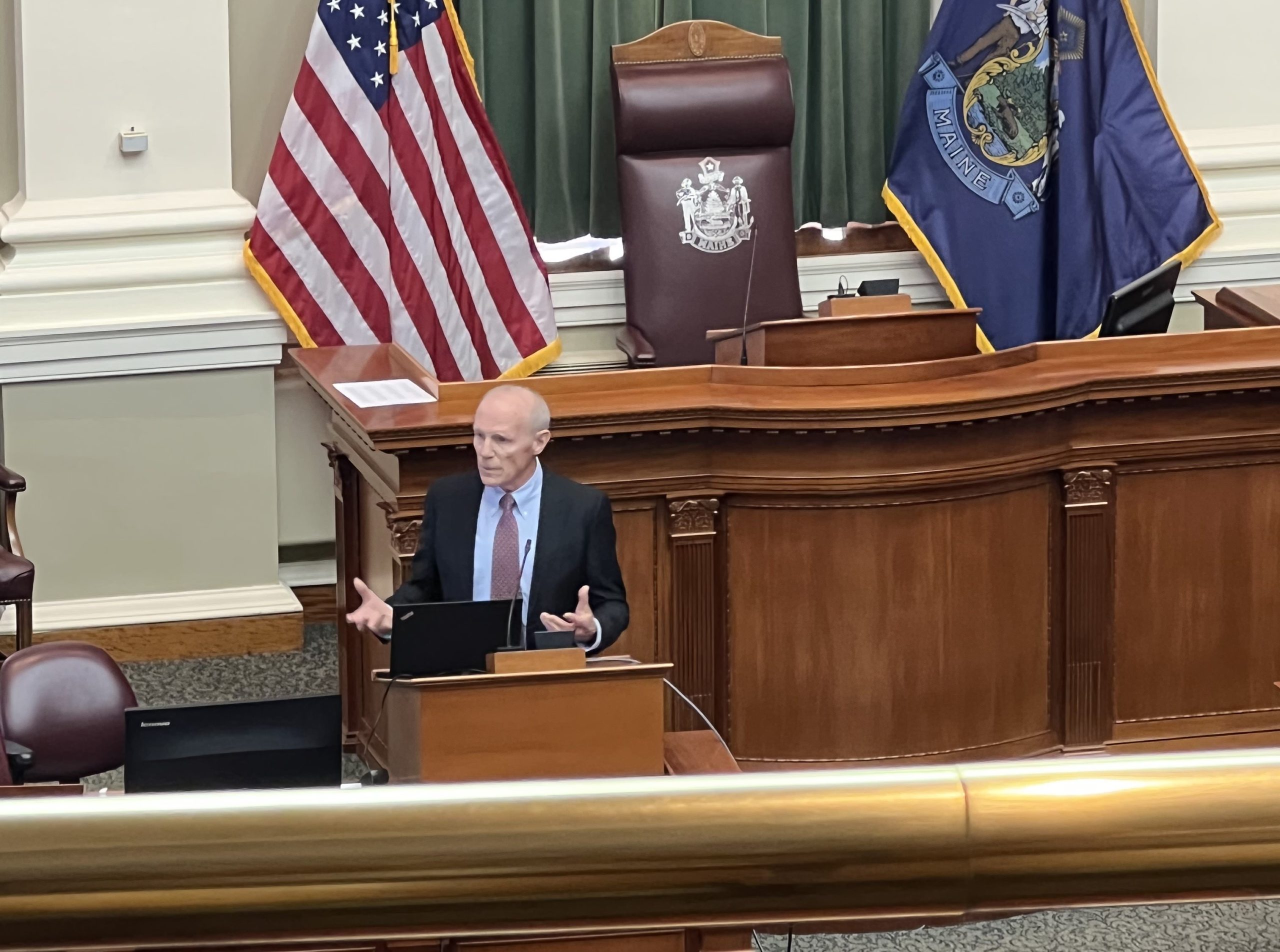 Copy of IMG_2210 image of man at podium speaking with american and maine flags behind him